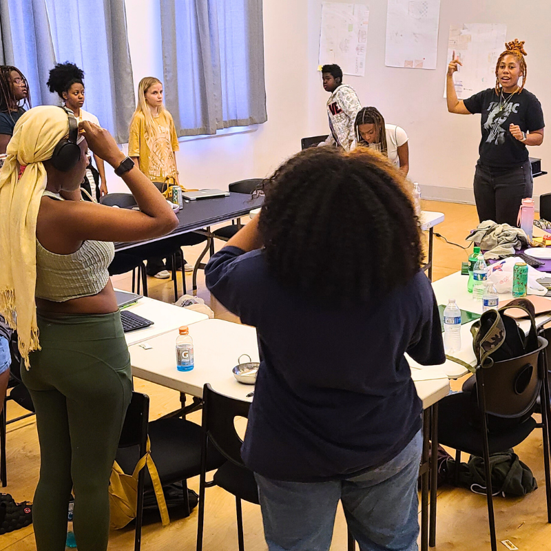 Participants in the Enrichment 2 Empowerment Program stand around a table listening to instructions.