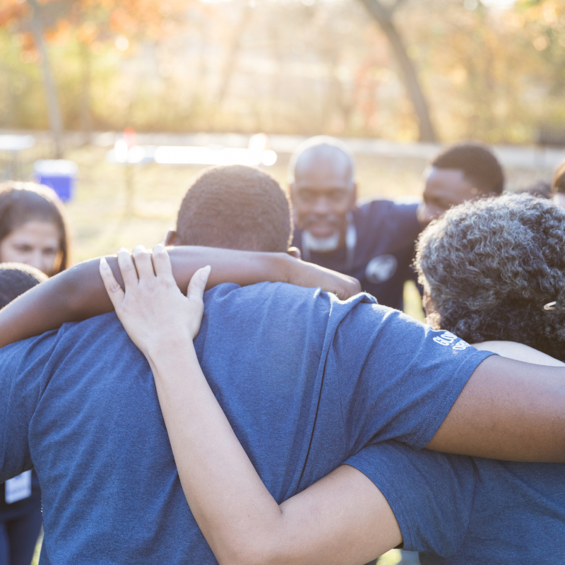 A diverse group of people stand in a circle with their arms around each other.