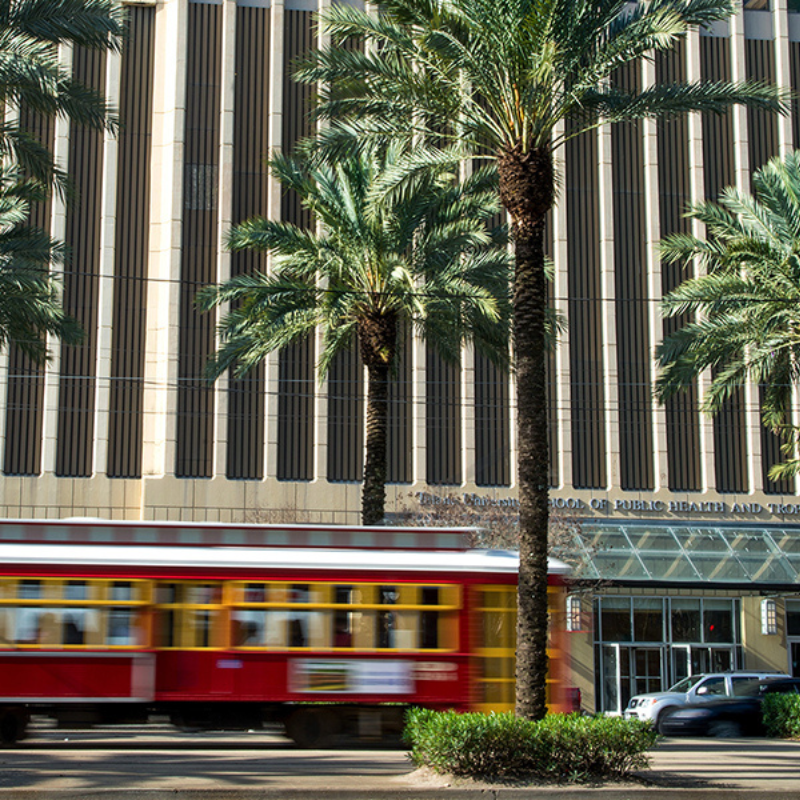 A red and yellow street car passes in front of the Tulane University School of Public Health on Canal Street.
