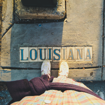 Photo of a person's feet standing on the sidewalk where Louisiana is spelled out in tiles