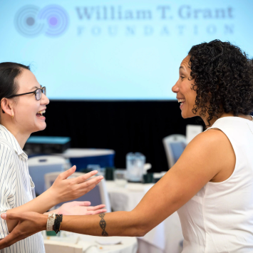 Two scholars connect with one another in front of a presentation screen that says "William T. Grant Foundation"